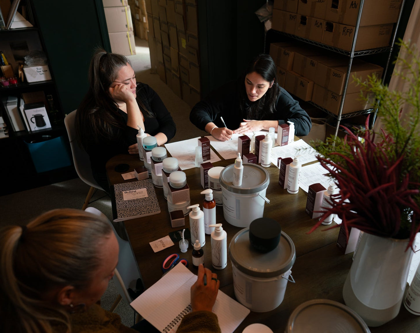 Three people sitting around a table with various items including bottles and containers.