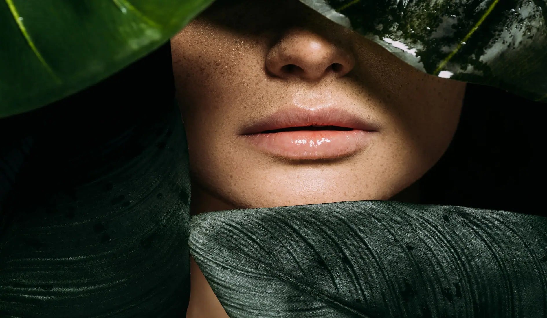 Female face peeking out from behind a large green leaf with a blurred natural background