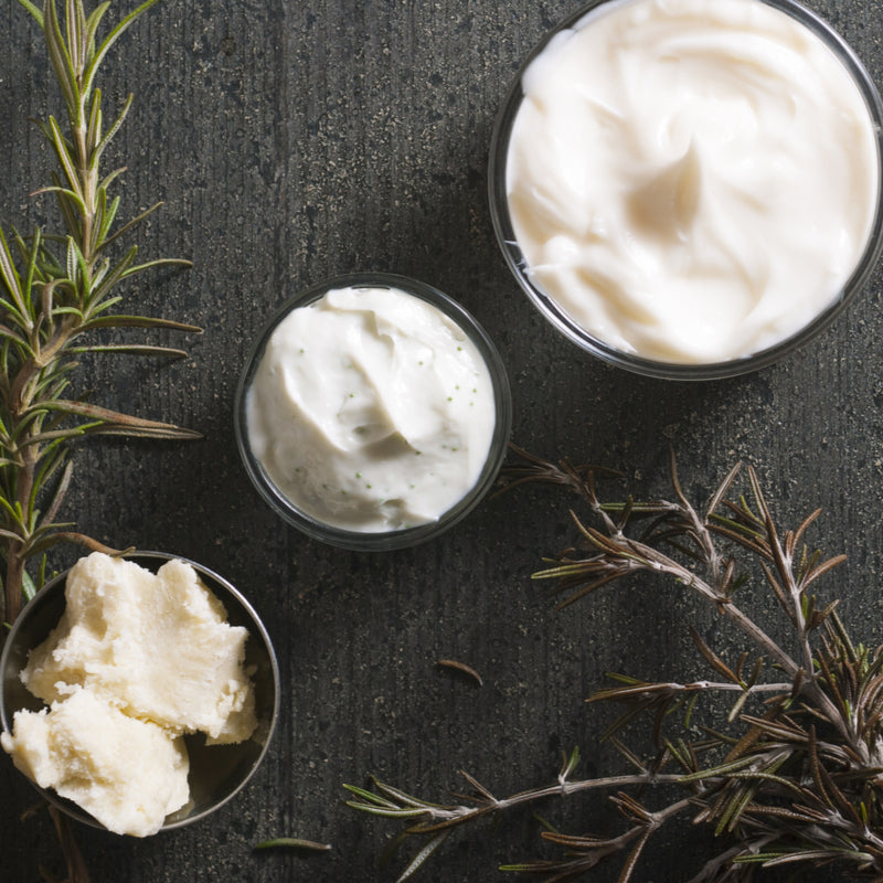 Three small bowls filled with a white cream on a dark surface with rosemary leaves.