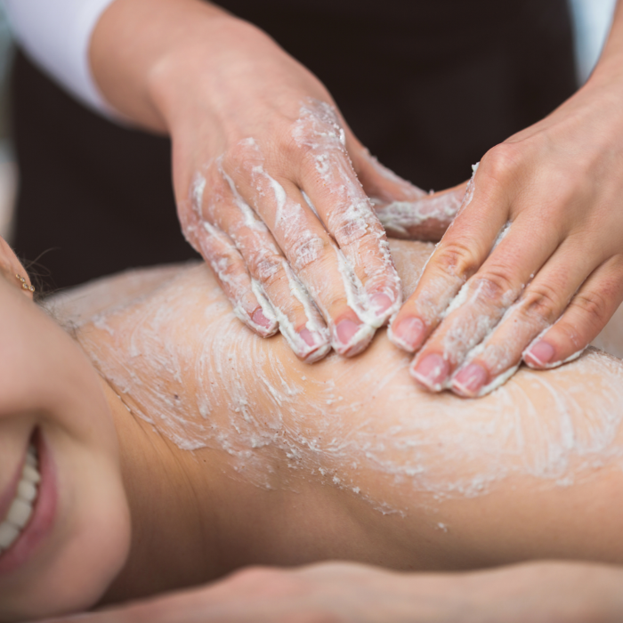 Person getting a skincare treatment with a body scrub on their shoulder.